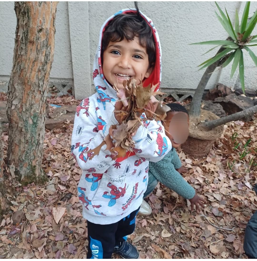 A happy child playing outdoors in the garden, holding autumn leaves