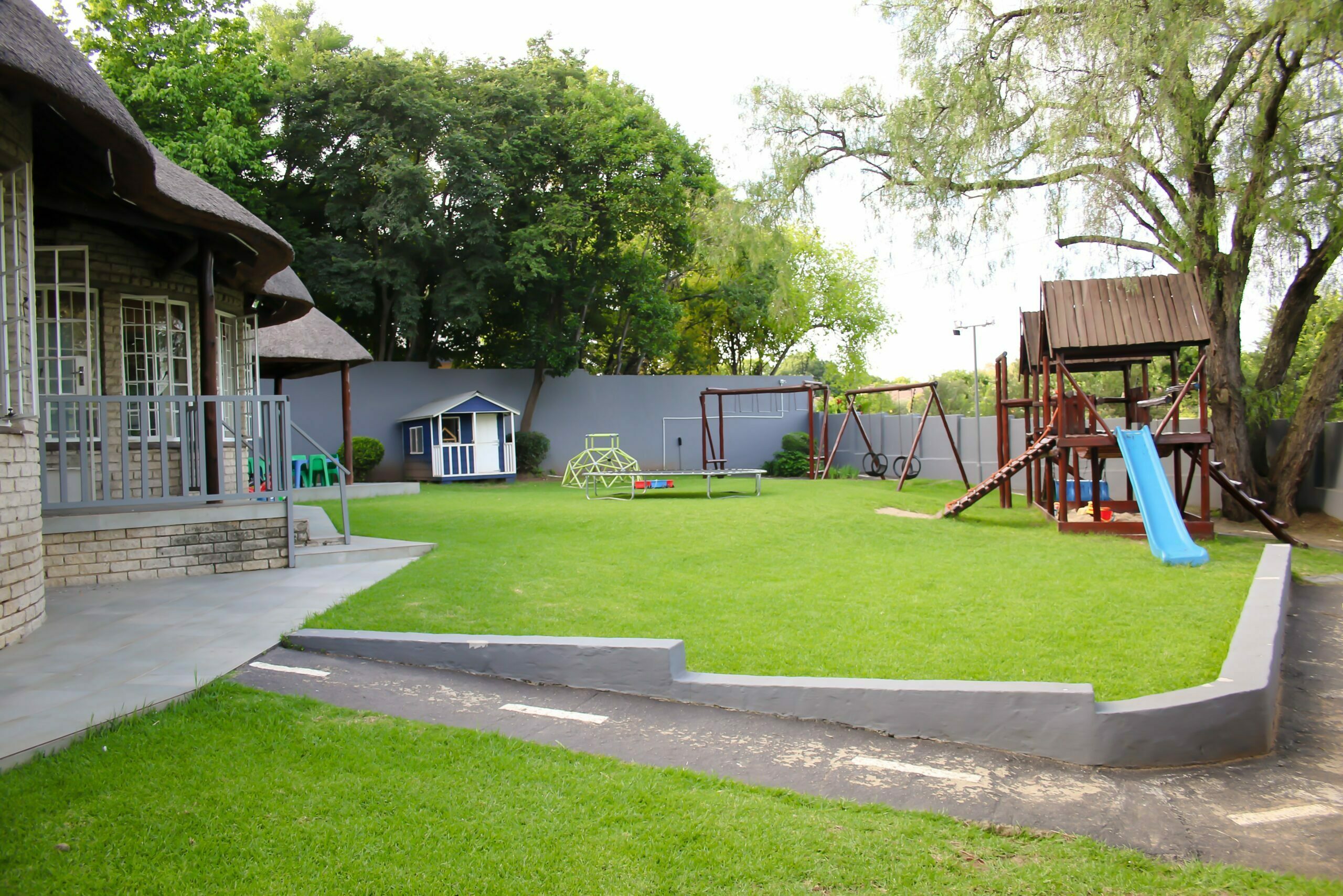 Outdoor garden with playhouse, swings and a slide beside the thatched-roof school
