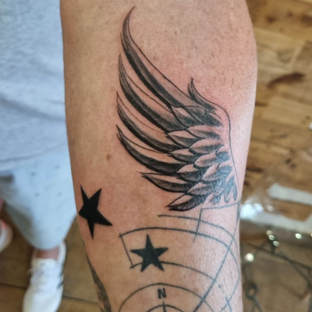 Black-and-grey angel wing tattoo on the forearm by Rob