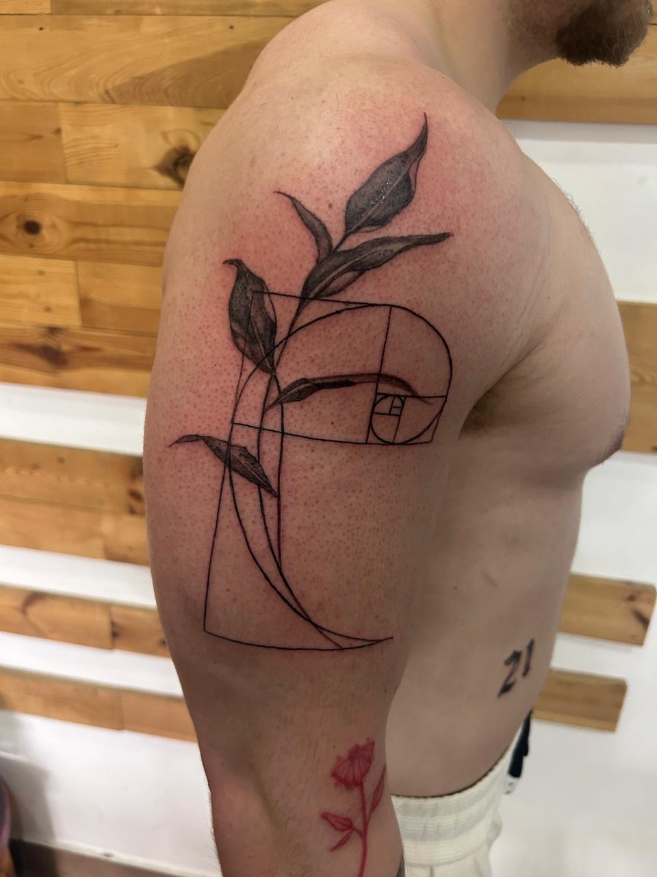 Fine-line botanical and golden-spiral tattoo on the shoulder by Ray