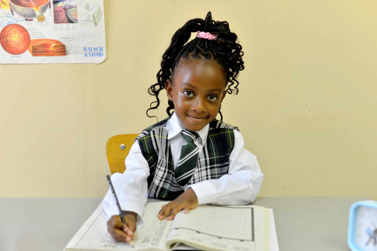 A Winners Academy pre-school pupil in tartan uniform smiling during a writing lesson